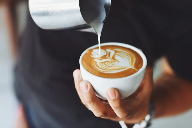 Barista gießt Milch für Latte Art in eine Kaffeetasse